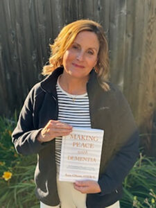 Occupational therapist holding the book “Making Peace with Dementia” in a garden, featured in the Sweet Basil Senior Care provider spotlight.